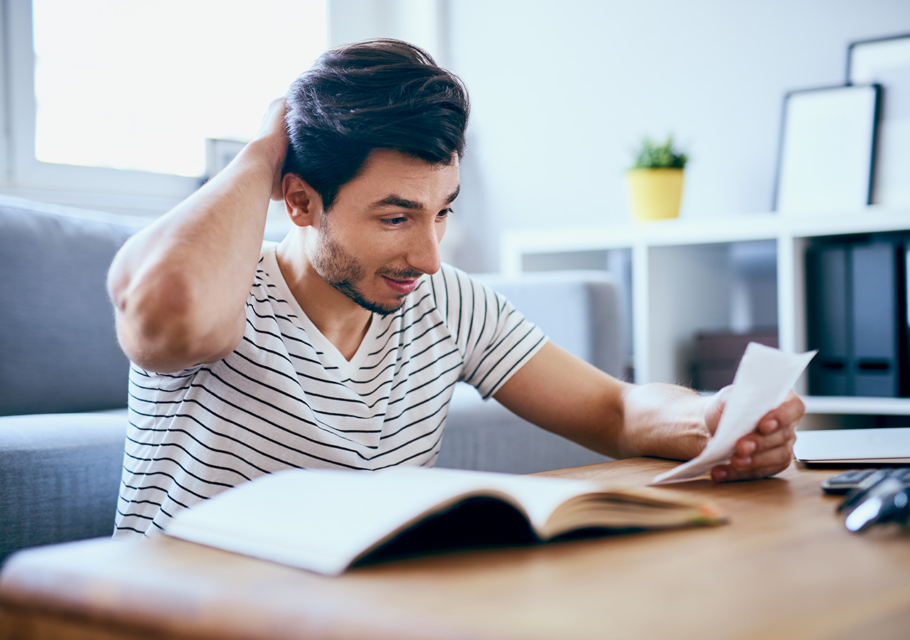 Junger Mann betrachtet Stromrechnung mit fragendem Blick