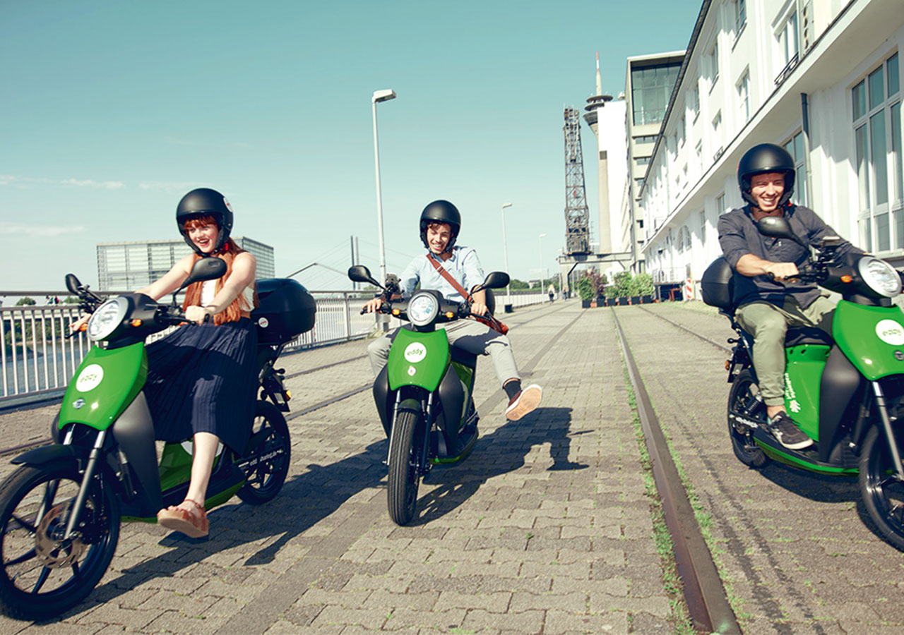Drei junge Menschen auf E-Rollern bei Sonnerschein im Medienhafen Düsseldorf