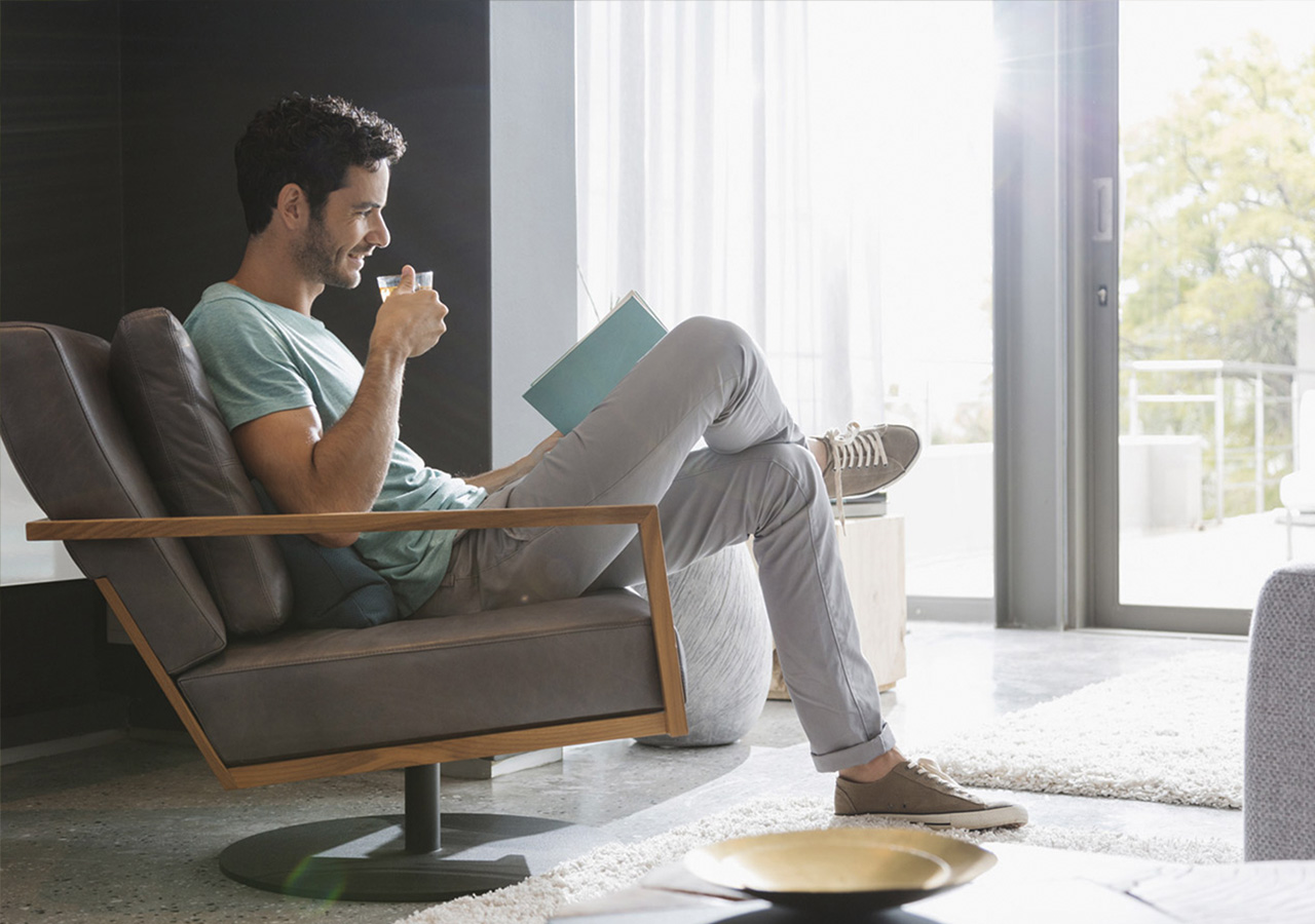 Ein junger Mann sitzt in einem Sessel, trinkt eine Tasse Tee und liest ein Buch