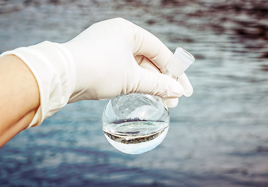 Trinkwasseranalyse: eine Hand im Gummihandschuh hält eine Wasserprobe