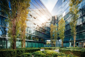 Bäume im Innenhof zwischen Gebäuden eines Unternehmens werden vom Sonnenlicht geküsst. © TommL / iStock Getty Images Plus via Getty Images