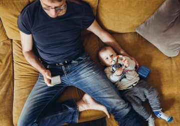 Mann sitzt mit Baby auf der Couch und passt am Handy seinen Abschlag an. © Westend61 via Getty Images