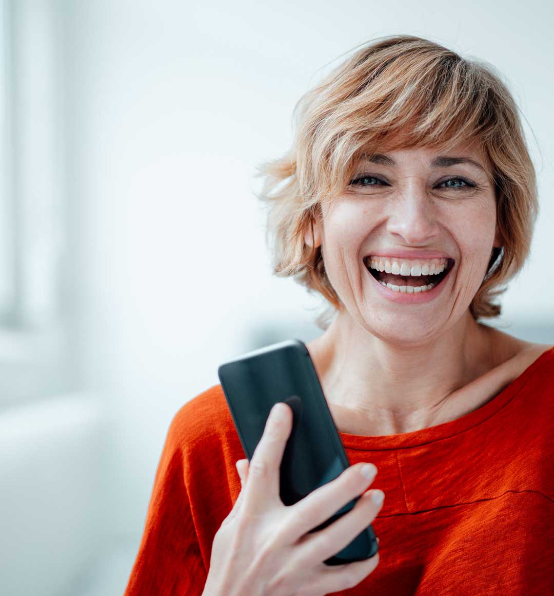 Eine lachende Frau mit einem Smartphone in der Hand. © Westend61 via GettyImages