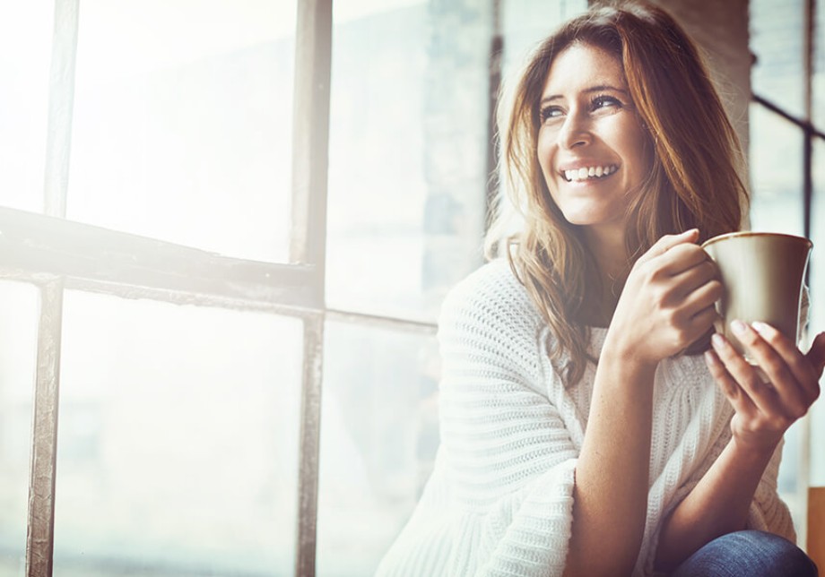 Rund ums Haus: Eine Frau mit einer Tasse Kaffee sitzt am Fenster und lächelt