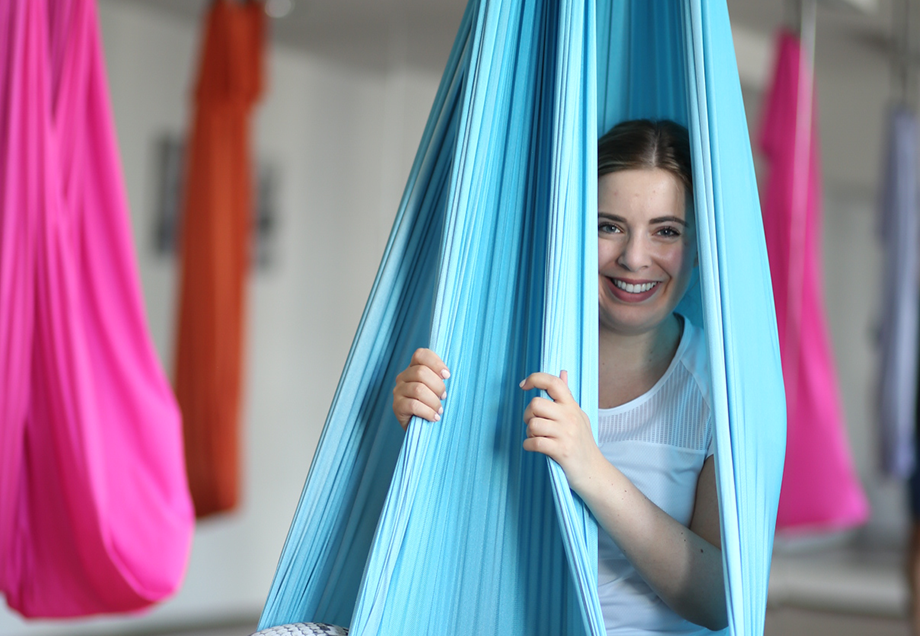 Yogastudio Yogamar: Katharina Bansemer sitzt lachend in einem von der Decke hängenden Yogatuch und verschwindet dabei fast ganz hinter dem Tuch.