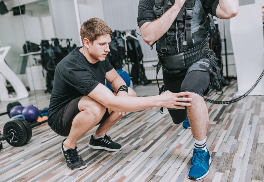 EMS-Training: Ein Trainer unterstützt seinen Kunden bei der Ausführung einer Sportübung.