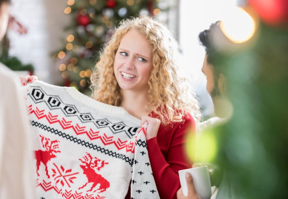 Schrottwichteln: Frau hält skeptisch ihren erwichtelten Weihnachtspullover