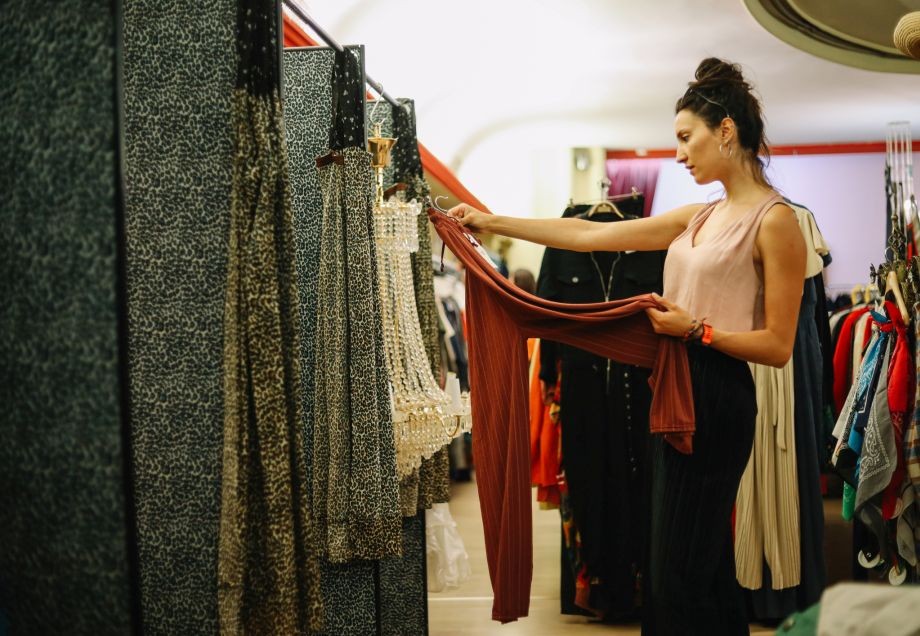 Eine junge Frau steht vor einer Umkleidekabine in einem Thrift Shop und begutachtet eine Hose.