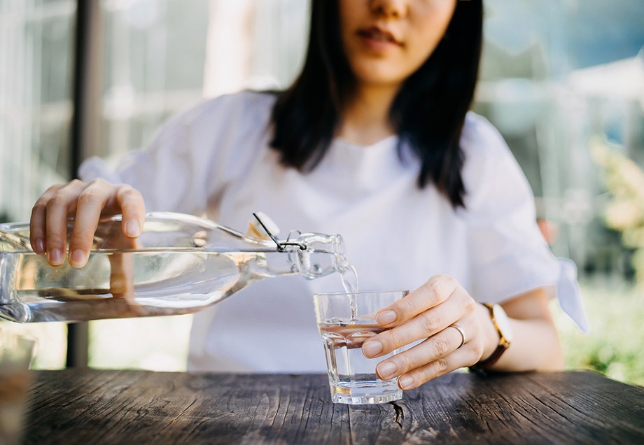 Wasser trinken: Eine Frau füllt ihr Wasser aus einer Flasche in ihr Glas. 