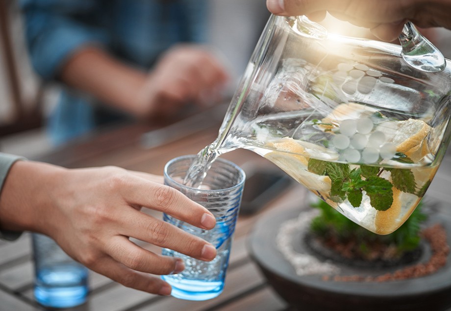 Wasser trinken: Einer Person wird Zitronenwasser mit etwas Minze in ein Glas geschüttet. 