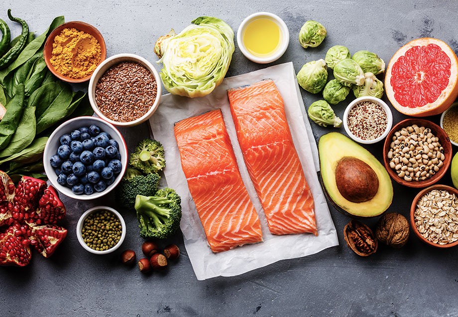 Eine Auswahl von frischen Zutaten wie Fisch, Avocado, Nüssen, Salat, Früchten und Gewürzen.