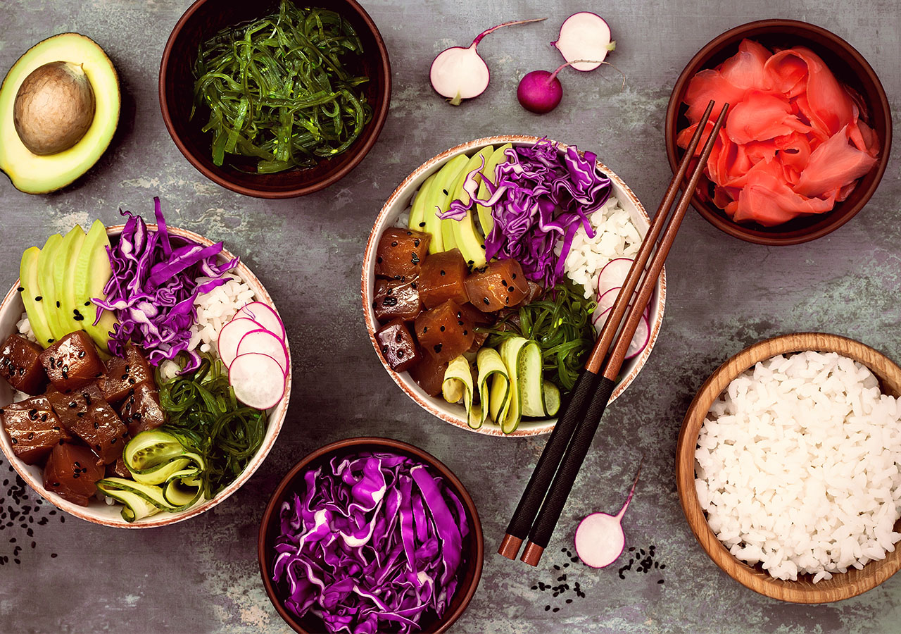 Zwei Poke Bowls – umgeben von den einzelnen Bestandteilen der Bowls. 