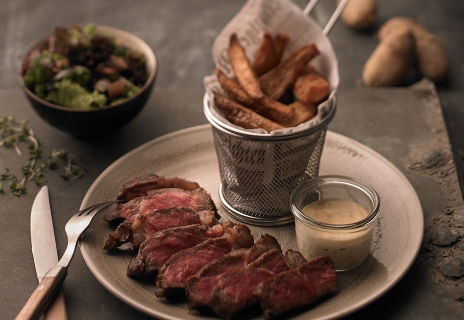 Eine Mahlzeit, bestehend aus Pommes, Fleisch, Mayonnaise und einer Schüssel Salat.