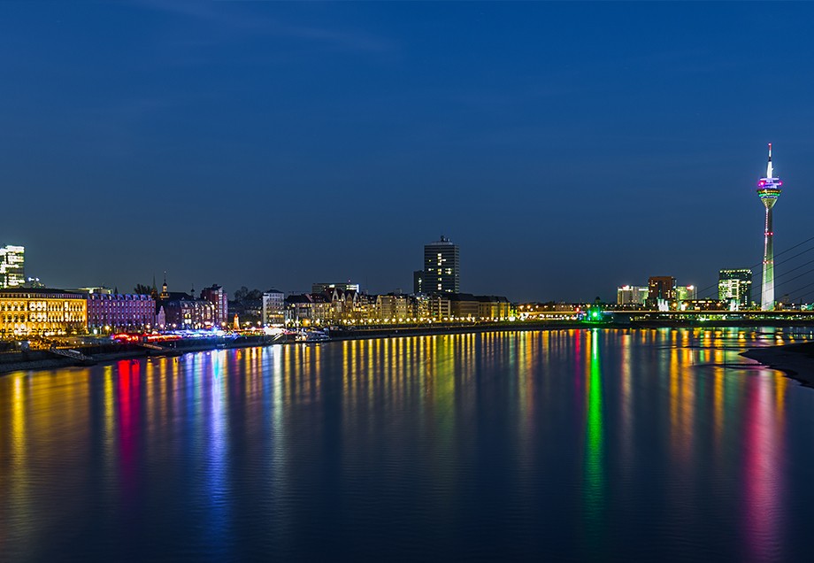 Bunte Lichter spiegeln sich im Wasser des Düsseldorfer Rheinufers.