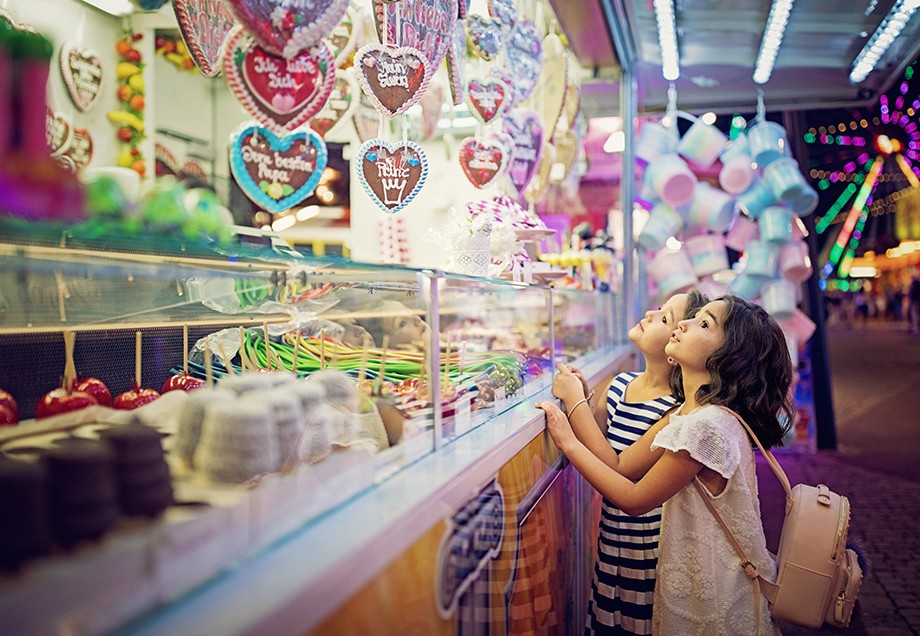 Zwei Mädchen bestaunen einen Süßigkeitenstand auf der Kirmes.