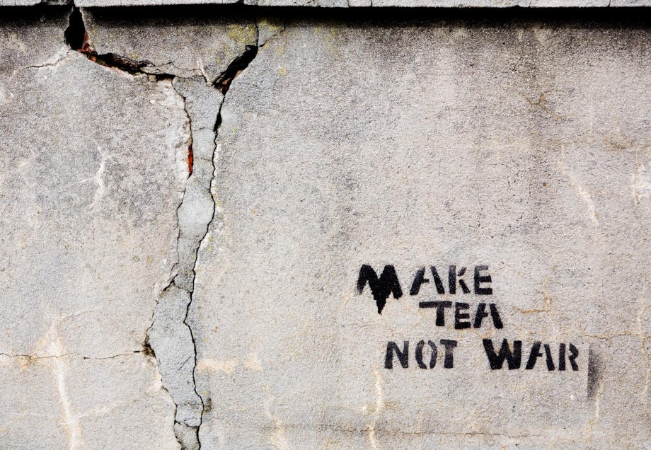 Ein Stencil mit dem Schriftzug „Make tea not war“ ziert eine rissige Mauer. 