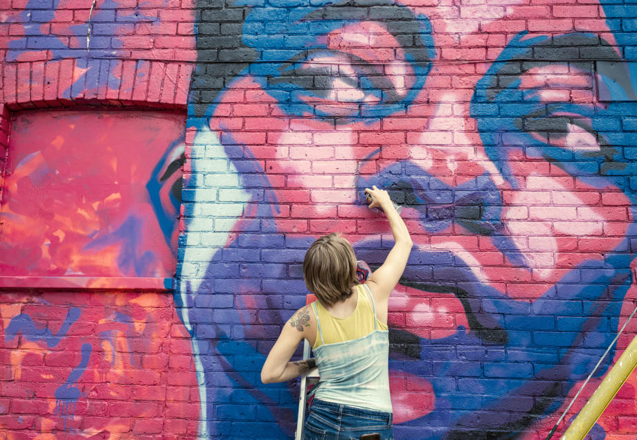 Eine junge Frau besprüht eine Hauswand mit einem bunten Graffiti. © FOTOGRAFIA INC. / E+ via Getty Images