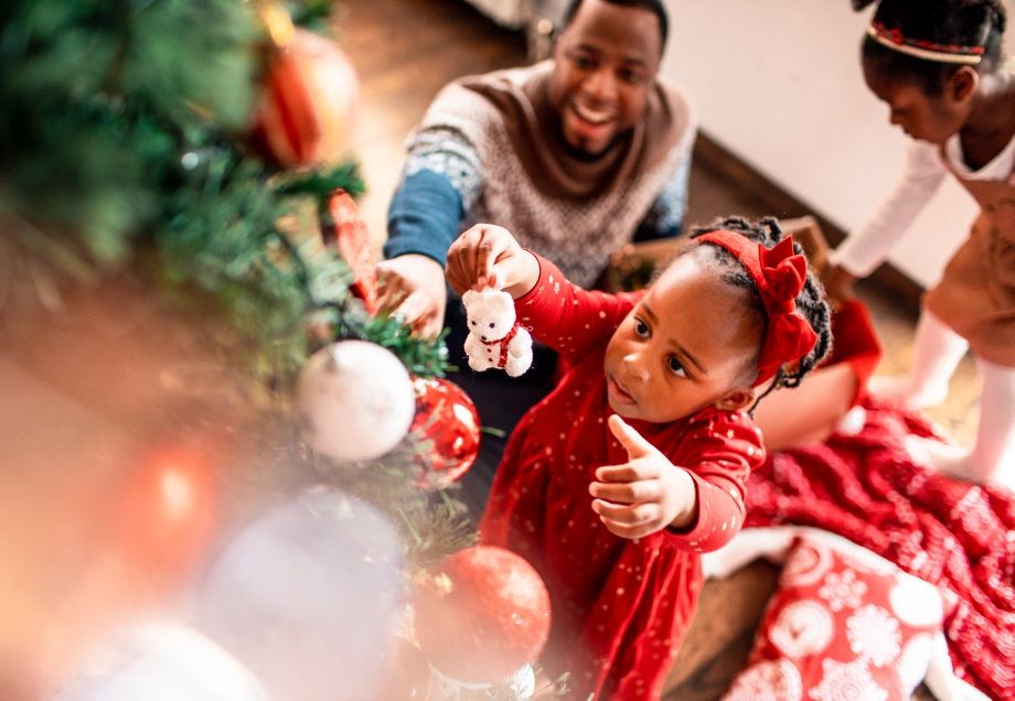 Weihnachten in anderen Ländern: Kleines Mädchen schmückt mit ihren Eltern den Weihnachtsbaum