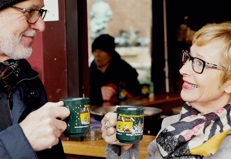 Mann und Frau in bestem Alter stoßen auf dem Weihnachtsmarkt mit Glühwein an.