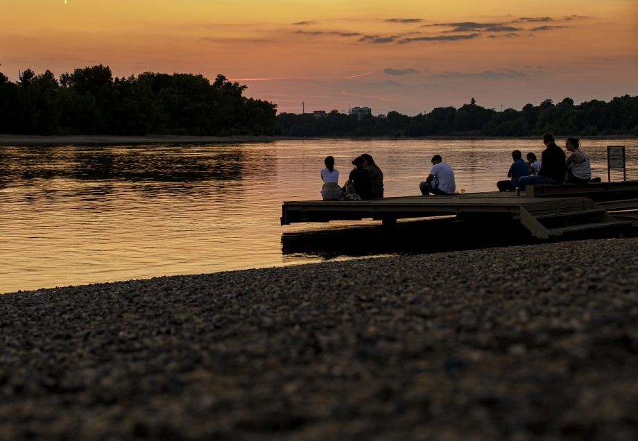 Menschen sitzen bei Sonnenuntergang auf einem Steg am Rhein in Benrath.
