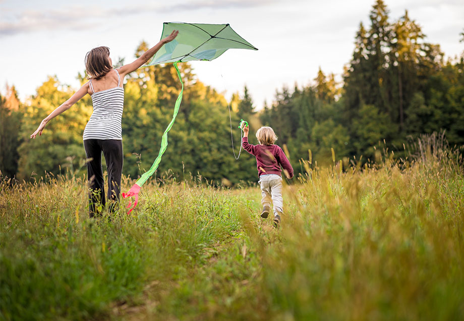 Ein Kind lässt im Grünen seinen Drachen steigen und seine Mutter hilft dabei. 