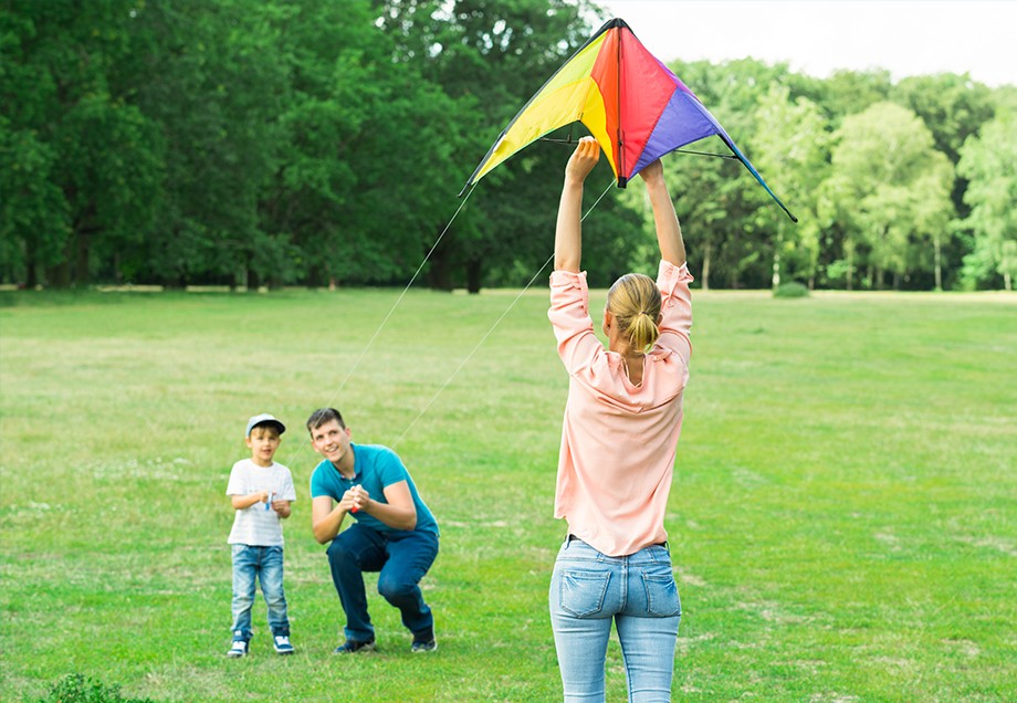Familie mit Mutter, Vater und Kind lässt Drachen steigen auf grüner Wiese im Park.