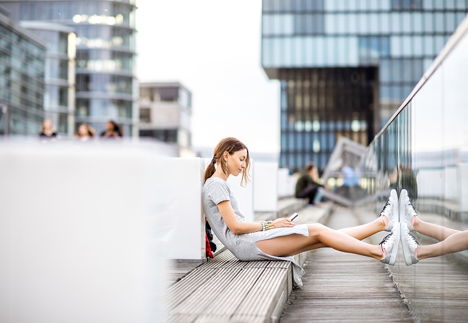 Eine junge Frau sitzt auf einer Holzbank im Düsseldorfer Medienhafen.