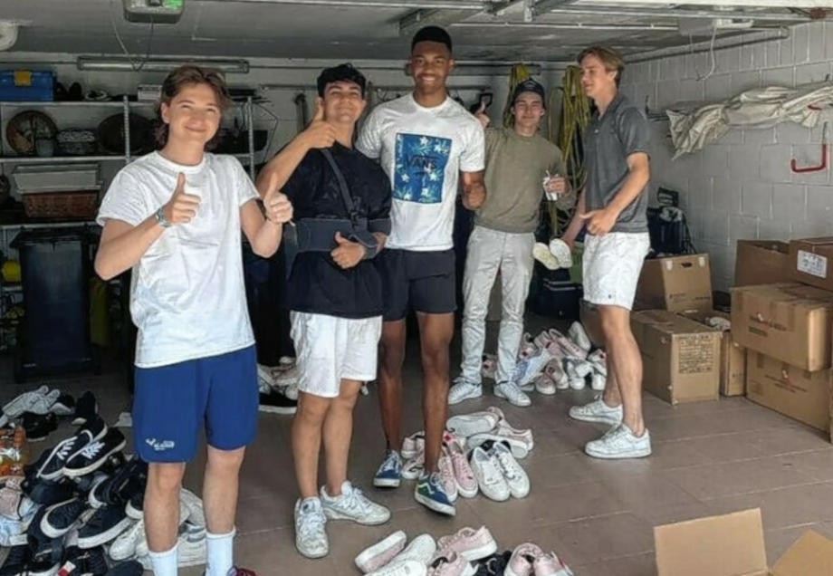 Fünf Schüler sind in einer Garage umgeben von gespendeten Schuhen und lächeln in die Kamera.