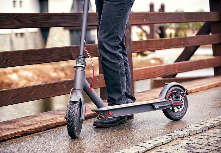 Schwarzer E-Tretroller mit roter Verkabelung steht auf dem Gehweg.