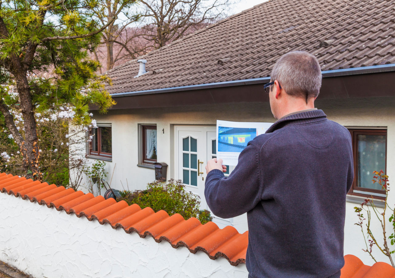 Energetische Sanierung: Ein Mann steht mit Energieanalyse vor einem Haus und schaut sich diese an.