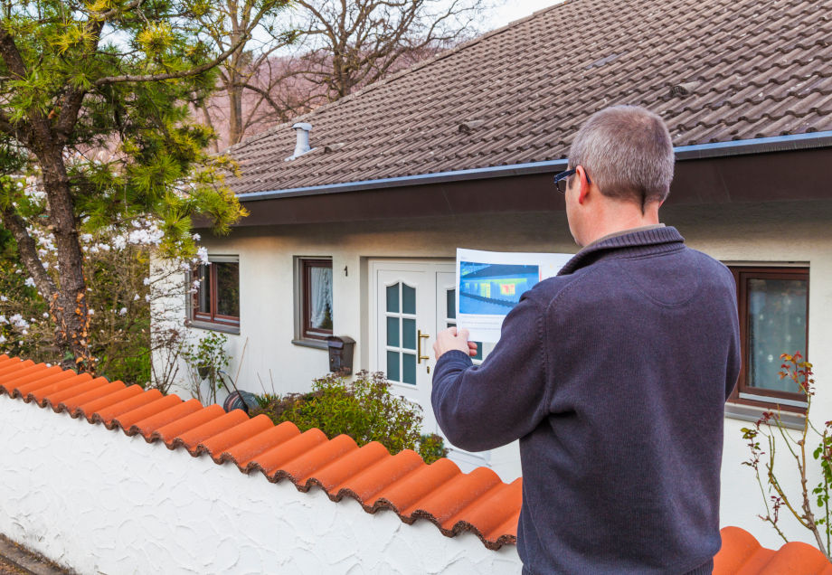 Energetische Sanierung: Ein Mann steht mit Energieanalyse vor einem Haus und schaut sich diese an.