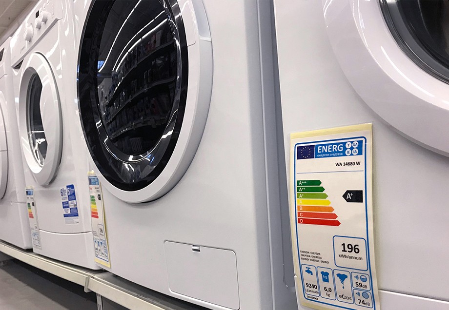 Ein älterer Mann studiert das bunte Energielabel auf einem Kühlschrank, der in einem Geschäft neben noch mehr weißer Ware steht.