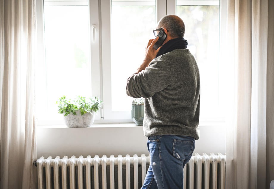 Gasarten: Ein Mann steht beim Telefonieren am Fenster und wärmt sich dabei an einer Heizung auf. 