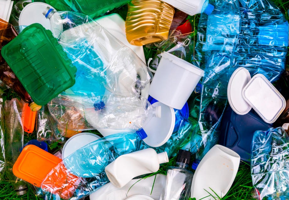 Unterschiedliche genutzte Plastikverpackungen wie Becher und Flaschen liegen auf Gras. 