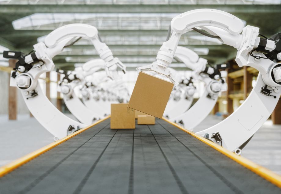 Eine Fabrik mit vollautomatisierter Produktionsstätte, an der Roboterarme Kisten greifen. 