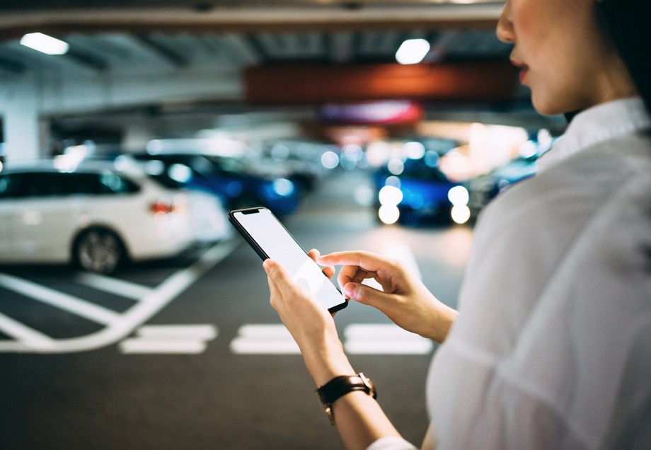 Mobilität der Zukunft: Eine Frau checkt ihr Smartphone, bevor sie zu ihrem Auto geht. 