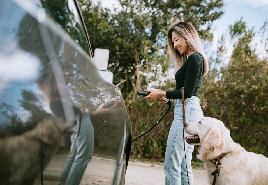 Eine Frau mit Hund lädt ihr Elektroauto auf. 