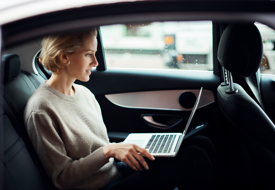 Eine Frau arbeitet auf der Rückbank eines Autos an ihrem Laptop