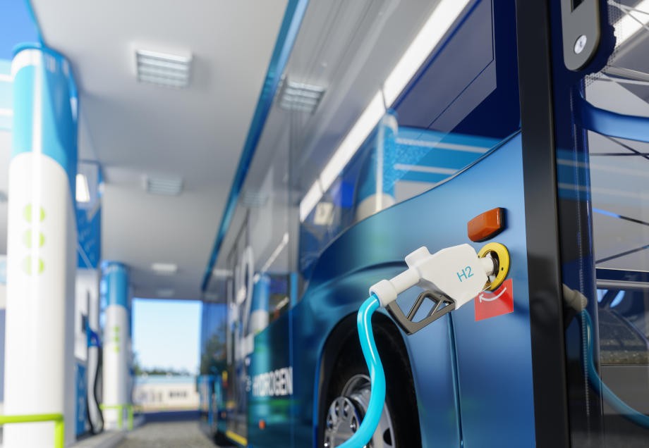Ein Wasserstoff-Bus ist an eine Zapfsäule einer Tankstelle angeschlossen, um Energie nachzuladen.
