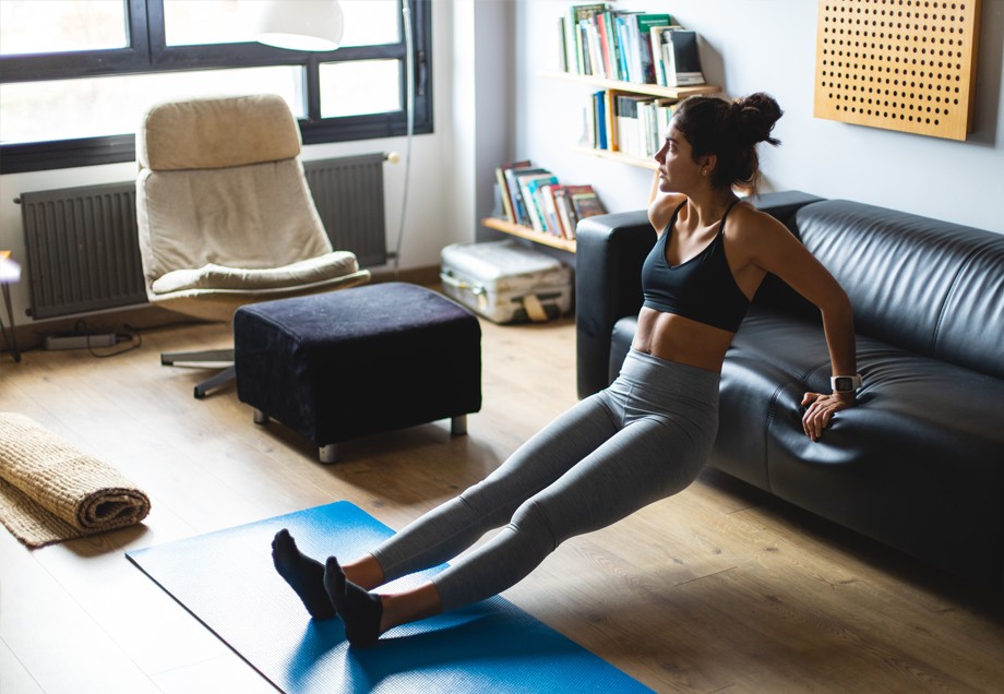 Sport zuhause: Mithilfe einer Couch trainiert eine junge Frau in ihrem Wohnzimmer.