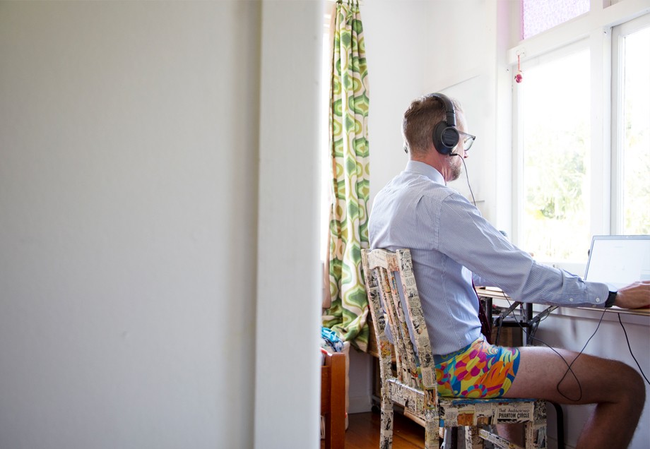 Blick von hinten auf einen Mann, der nur mit Businesshemd und buntgemusterten Boxershorts zuhause am Laptop arbeitet.