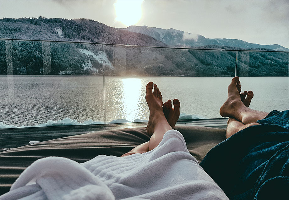 Das ist Hygge: Ein Paar entspannt in Bademänteln auf einer Sonnenterrasse mit Blick auf See und Berge.