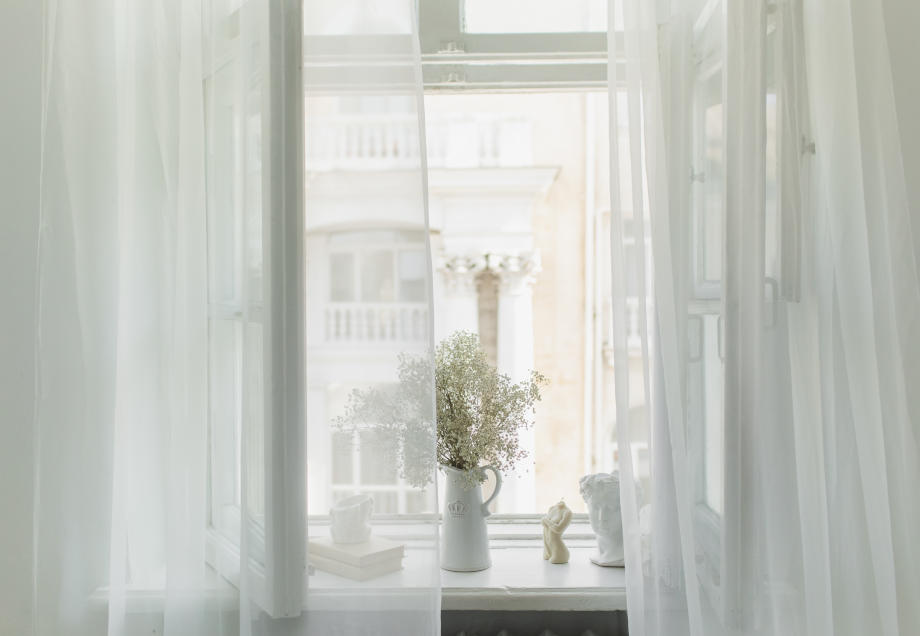 Richtig Lüften gegen Schimmel: Ein helles Zimmer mit transparenten Vorhängen und einem offenen Fenster. 