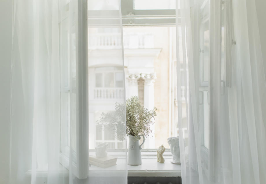 Richtig Lüften gegen Schimmel: Ein helles Zimmer mit transparenten Vorhängen und einem offenen Fenster.