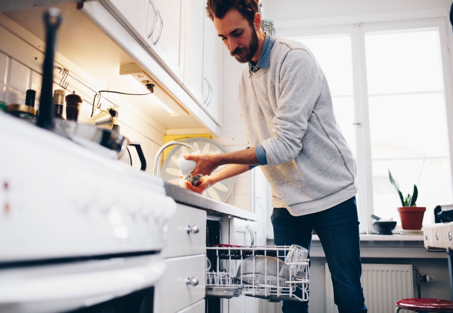Spülmaschine einräumen: Ein Mann entfernt grobe Essensreste.