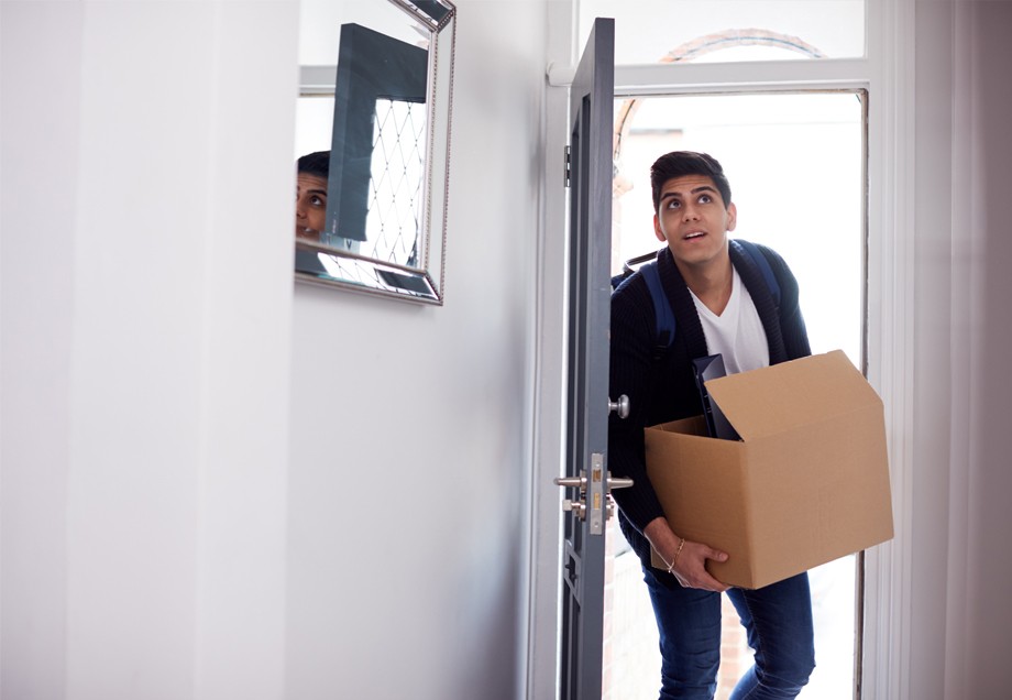 Ein junger Mann betritt mit einem Umzugskarton in Händen eine neue Wohnung.