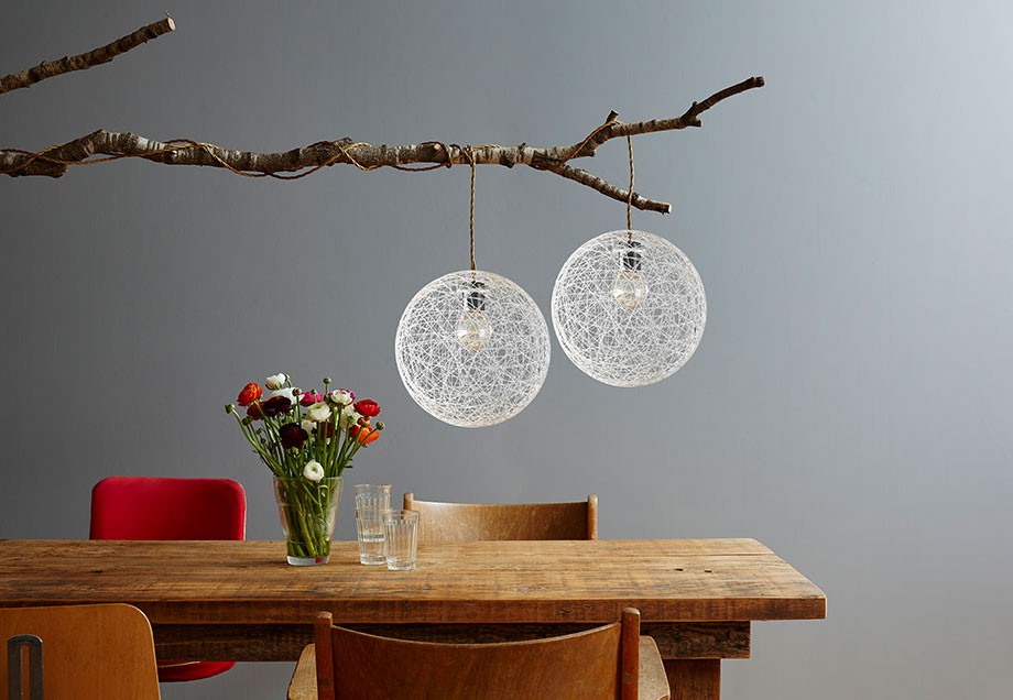 Zwei Fadenlampen, die an einem Ast über einem Esstisch hängen. Auf dem Tisch stehen ein paar Trinkgläser und ein Blumenstrauß in einer Vase.