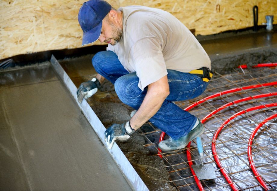 Ein Handwerker stellt die Verlegung einer Fußbodenheizung fertig, indem er den Estrich aufbringt.