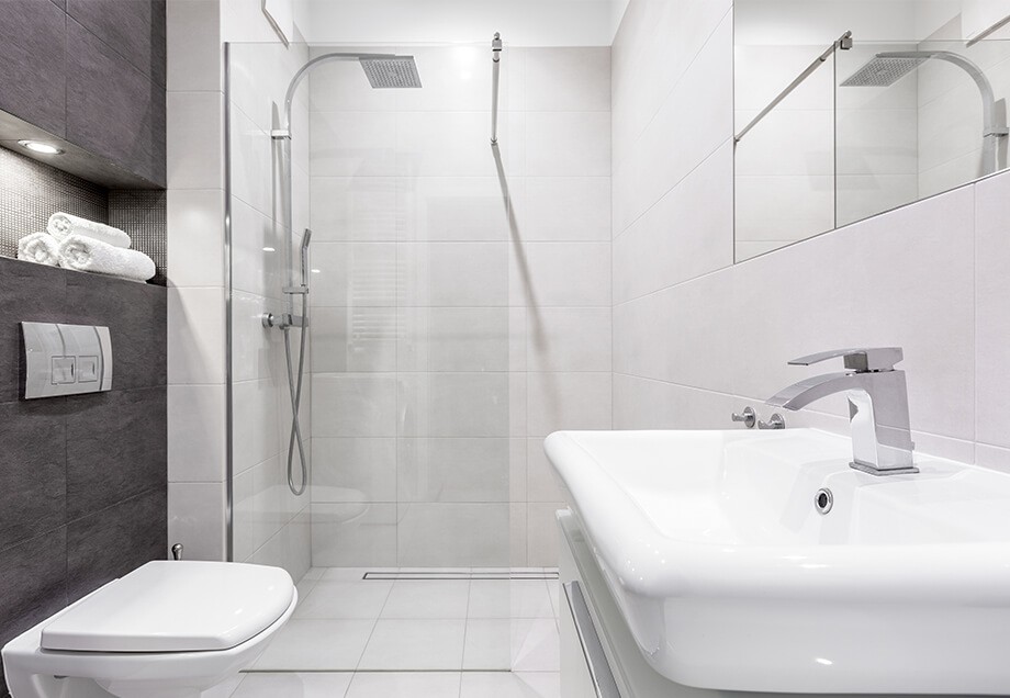 Ein helles Badezimmer mit einer dunkelgrauen Wand aus Fliesen und drei weißen Wänden wirkt ruhig und aufgeräumt. 
