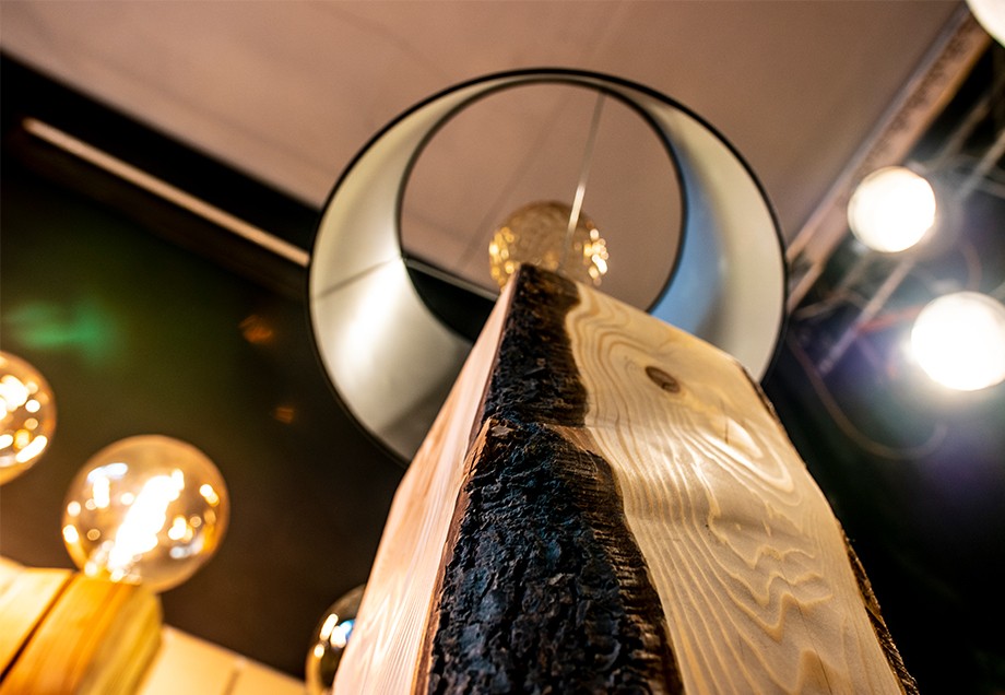 Blick vom quaderförmigen Holzfuß einer Lampe zu Glühbirne und textilem Lampenschirm.